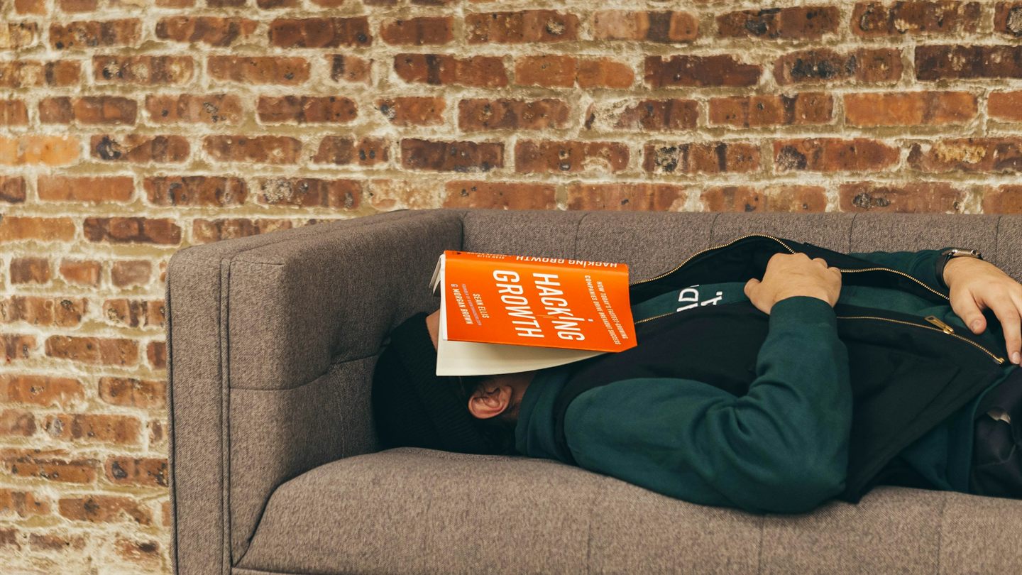 A person asleep on a couch with the book Hacking Growth covering their face